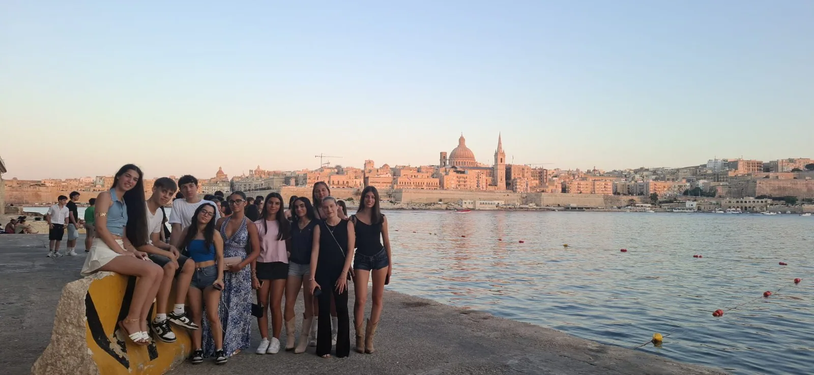 Students by the waterfront with Valletta’s skyline at sunset